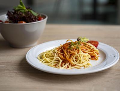 Plate of spaghetti with a salad in the background