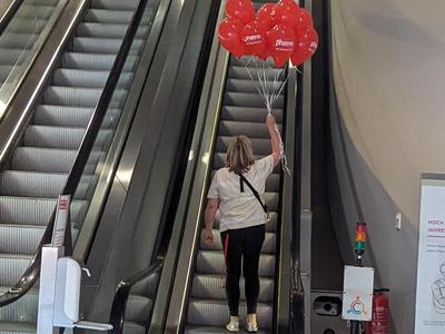 Frau mit Luftballons auf Rolltreppe