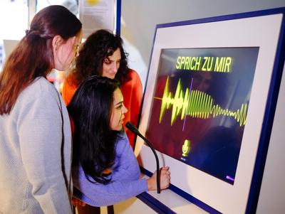 Schülerinnen an Mikro betrachten visualisierte Schallwellen auf einem Bildschirm